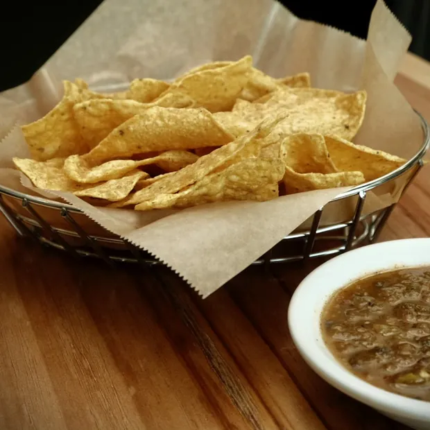 Tortilla chips in a wire basket with a bowl of salsa.