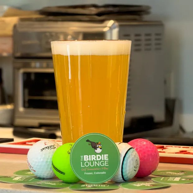 A cold pint on the bar with golf balls and a Birdie Lounge coaster